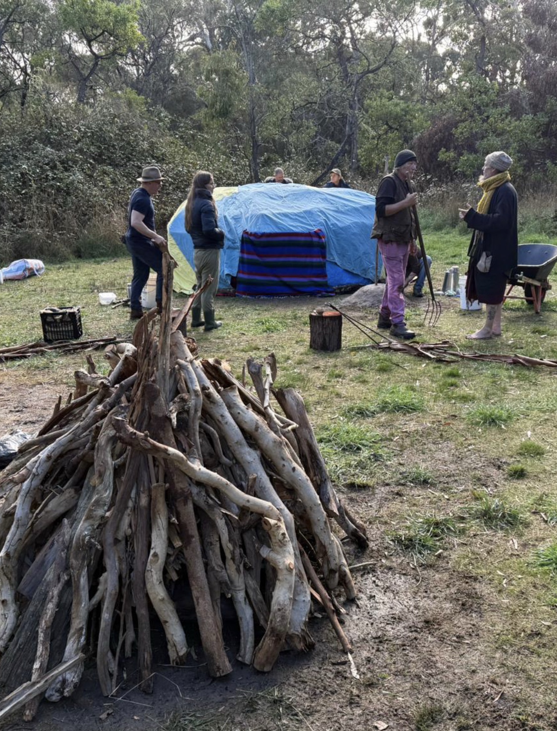 People preparing the covered Spirit Lodge and firewood together at The Farm for Wellbeing.